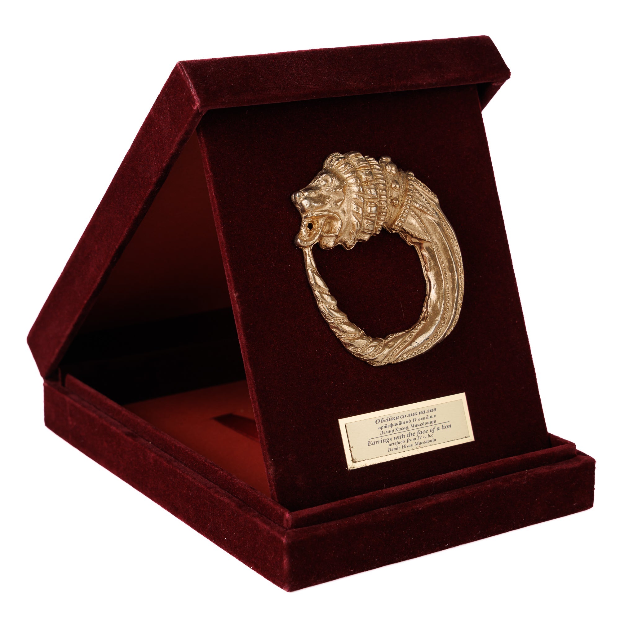 Луксузна бордо кадифена кутија поставена како држач, откривајќи автентична реплика на античка македонска обетка со лавовска глава од ВЕКОВИ.