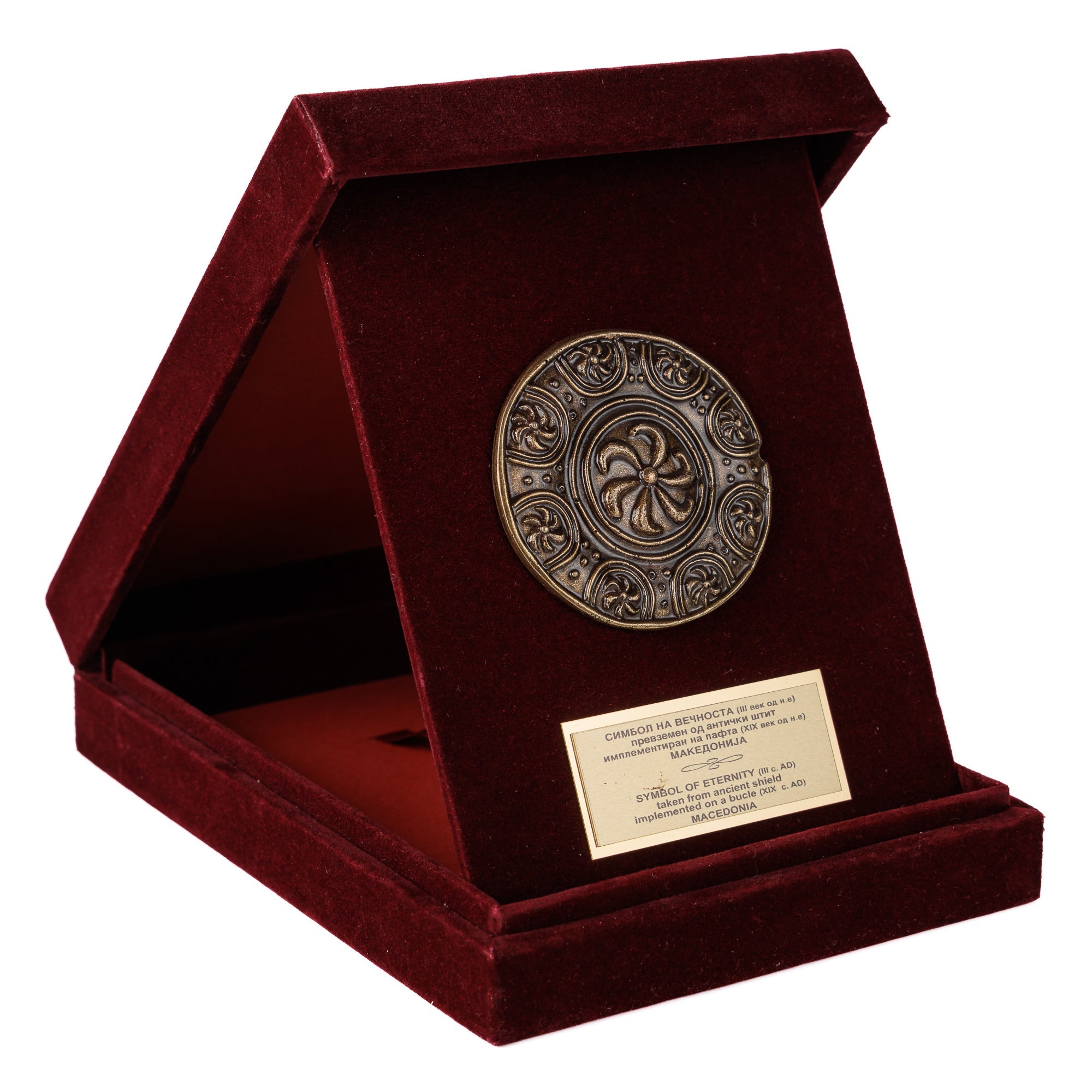 Луксузна бордо кадифена кутија поставена како држач, откривајќи моќен бронзен релјеф на античкиот Македонски Штит - Симбол на Вечноста од ВЕКОВИ.