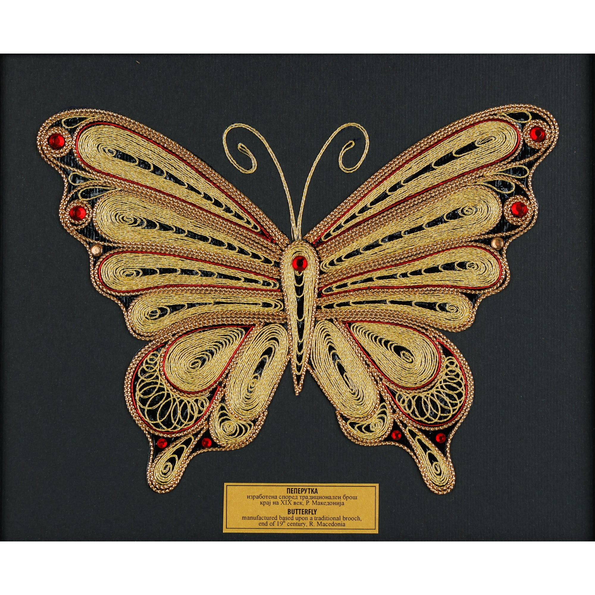 Детален приказ на симетричните крилја на филигранската пеперутка изработена од златна срма и црвени камења.
